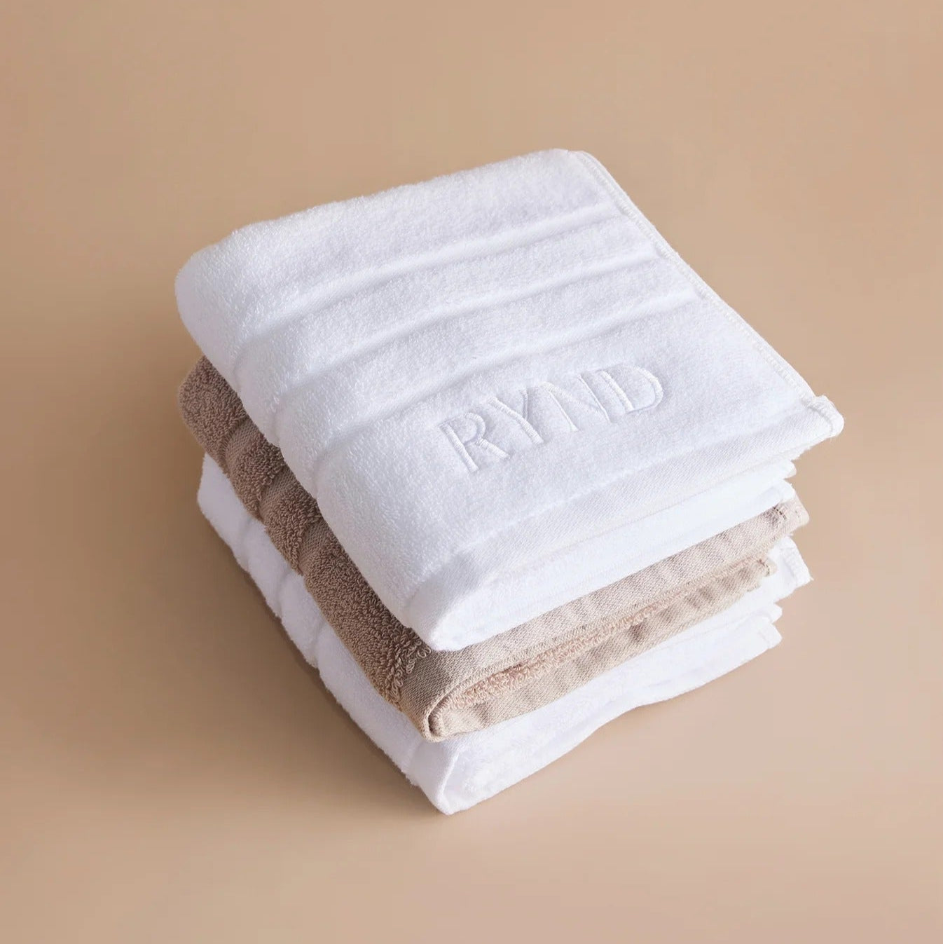 Stack of white and beige towels with 'Rynd' branding on a beige background