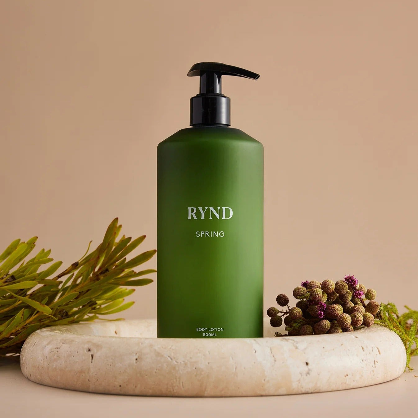 Green bottle labeled 'RYND' on a beige surface with natural elements.