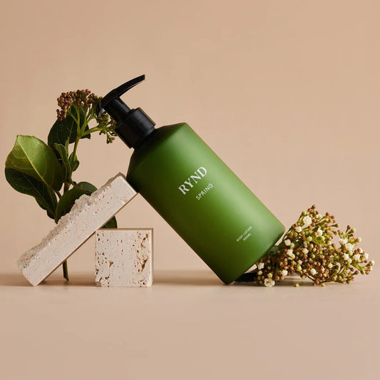 Green bottle with pump labeled 'RYND' on a beige background with plants.